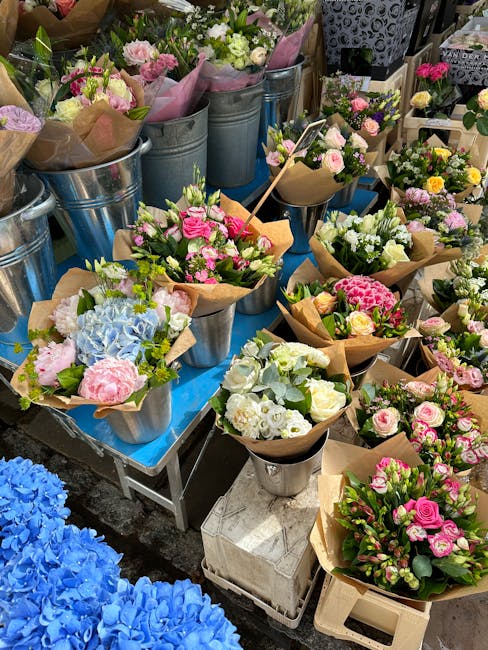 A display of fresh flower bouquets arranged in metal buckets and wrapped in brown paper, featuring a variety of pastel-colored blooms including pink roses, white hydrangeas, light green hydrangeas, an