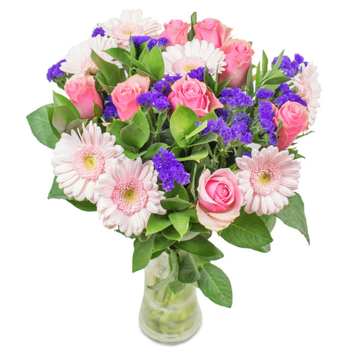 Displayed against a simple white background, this striking bouquet is a visual celebration of pink and purple, expertly arranged by the team at Flowers Marks Gate. The focal point is an enticing blend of seven to nine pink roses, their petals plush and either tightly curled or just beginning to open in elegant spirals. Alongside, five to seven pale pink gerbera daisies spread wide, their generous size and radiating petals serving as a gentle contrast to the roses' classic form. Clusters of electric purple statice or limonium weave through the arrangement, introducing lively texture and tonal depth reminiscent of late blooms found near Mayesbrook Park. The lush green foliage acts as a vibrant base, offering density and a touch of wild freshness, as if gathered from local hedgerows. Presented in a tall, clear glass vase with crisp water visible and sturdy stems on display, the bouquet feels distinctly fresh - ready for prompt delivery to homes and offices throughout Marks Gate. Whether the sentiment is birthday joy, a Mother's Day tribute, or simply a decorative centrepiece for a living room near Chadwell Heath, this composition exudes celebration, affection, and local floral artistry.